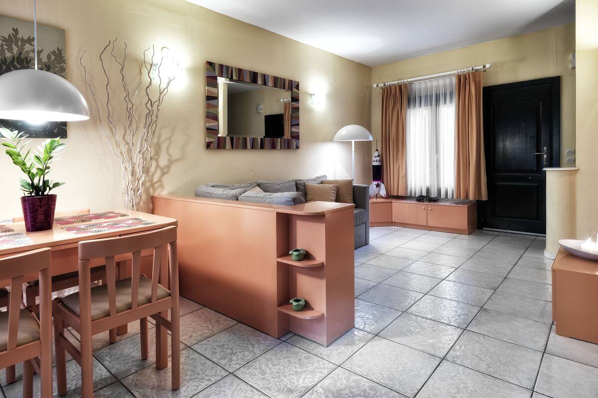 Ein modernes Wohnzimmer mit einer Couch, einem Esstisch, Stühlen, einer Topfpflanze, einem Spiegel und einer schwarzen Tür.