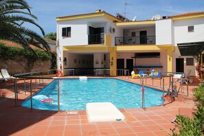 A swimming pool with a lifeguard chair, a diving board, and a lounge area with chairs and umbrellas.