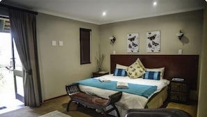 Quarto com cama, um banquinho, uma cadeira, mesa de cabeceira e obras de arte nas paredes.