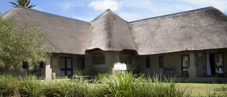 A building with a thatched roof, a covered outdoor seating area, and a paved entrance.