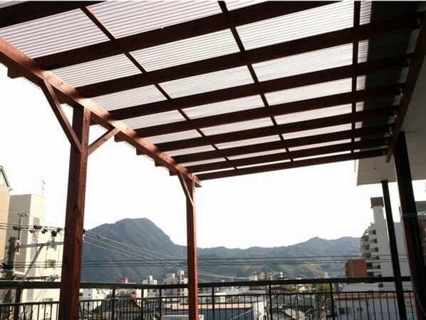 A covered outdoor area with a metal roof and wooden beams, overlooking a cityscape and mountains. - Guesthouse Danran (Beppu)