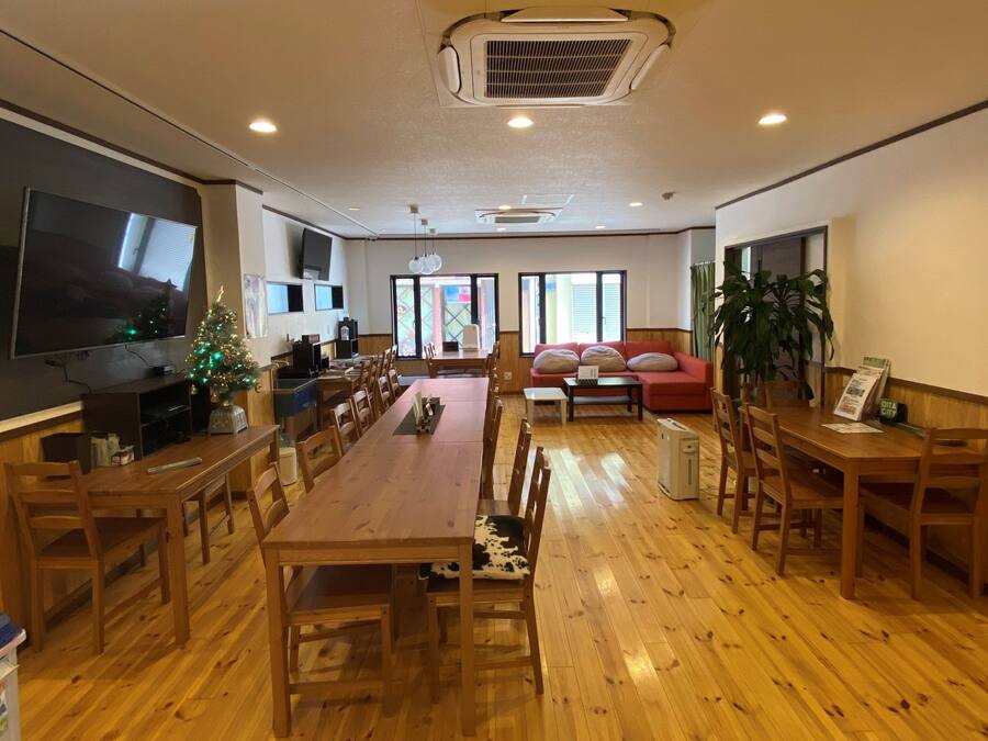 Uma sala de estar ampla com uma grande mesa de jantar de madeira, um sofá vermelho e uma televisão.