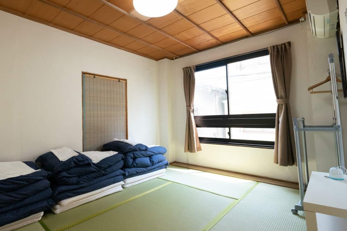 A room with two beds, a window with curtains, a radiator, and a small table with a cup.
