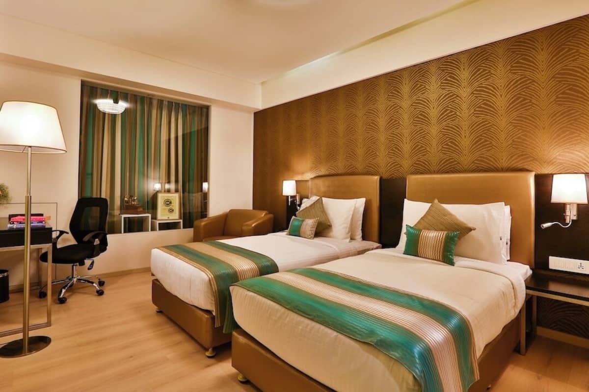A hotel room with two beds, a desk, a chair, and a nightstand with lamps.