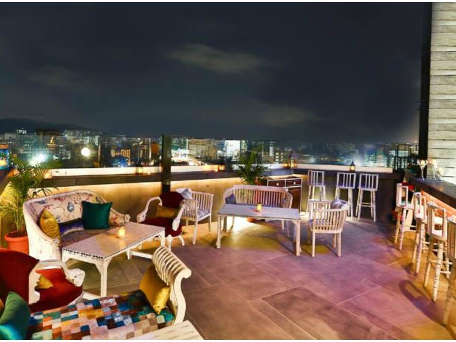 Terraço no telhado com área de estar, bar e vista noturna da cidade.