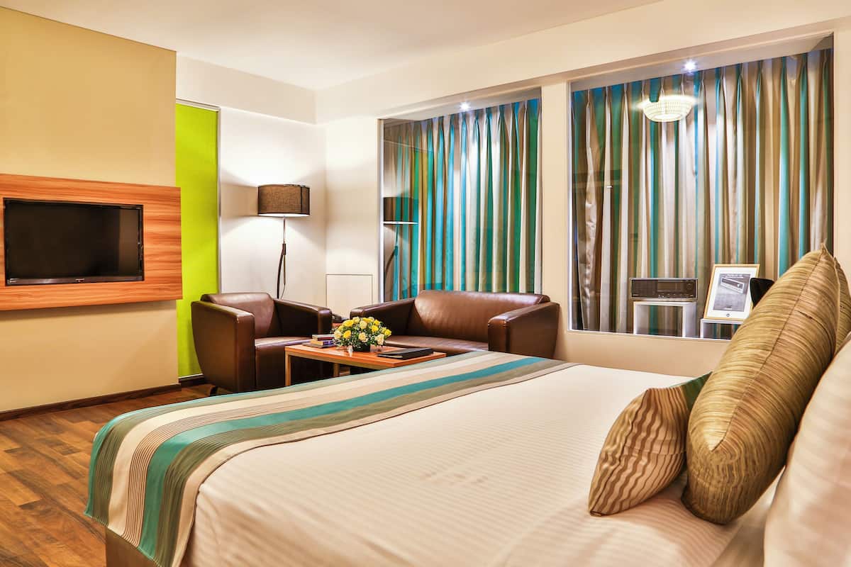 A hotel room with a bed, a desk with a lamp, a TV, and a window with curtains.