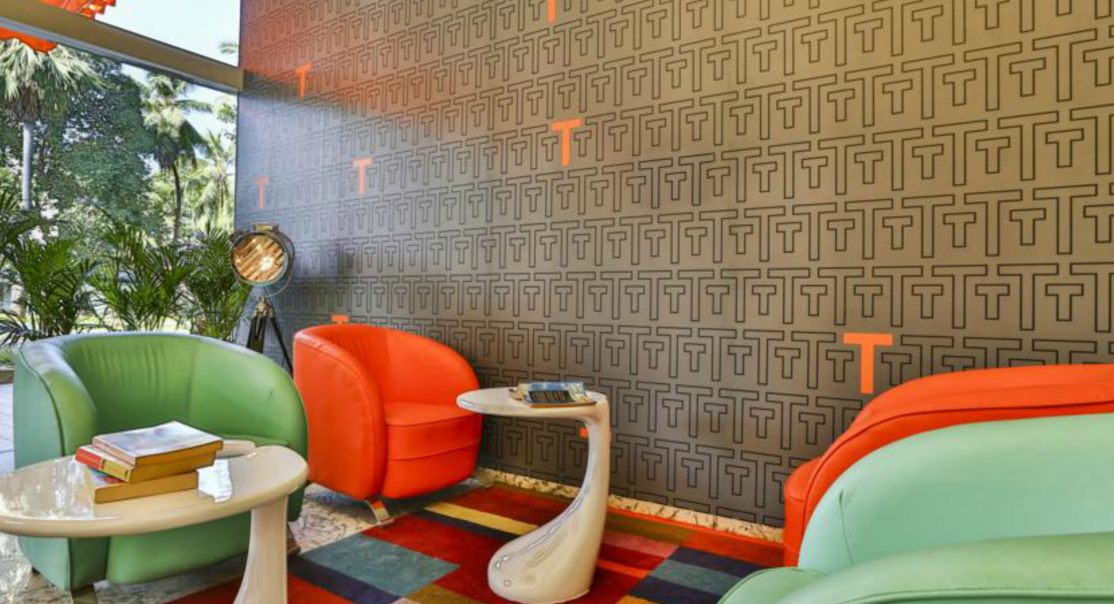 A room with a patterned wall, green and orange chairs, a small table, and a colorful rug.
