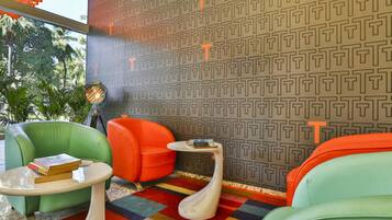 A room with a patterned wall, green and orange chairs, a small table, and a colorful rug.