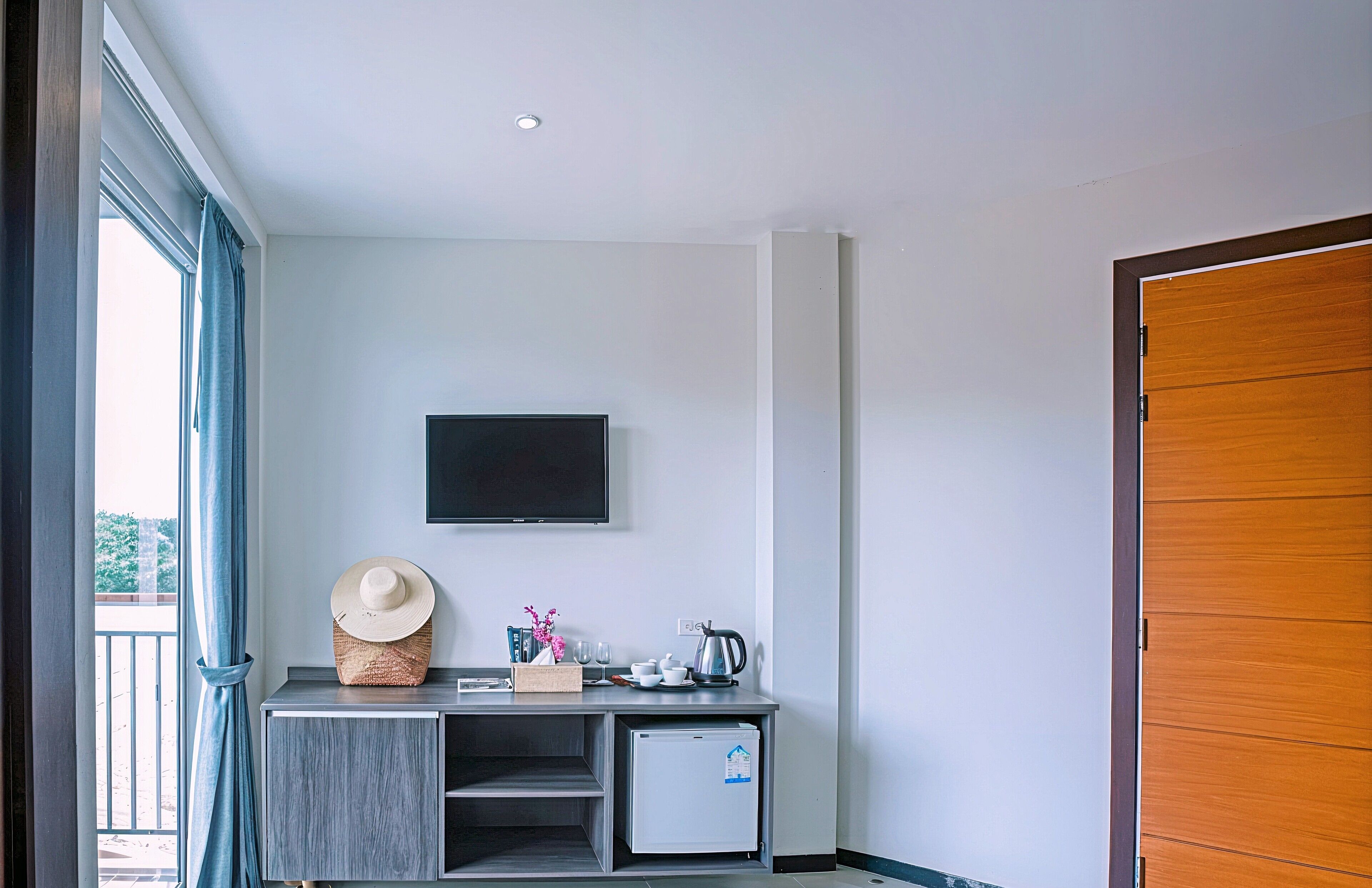 A compact room with a small kitchenette, a flat-screen TV mounted on the wall, and a wooden door.