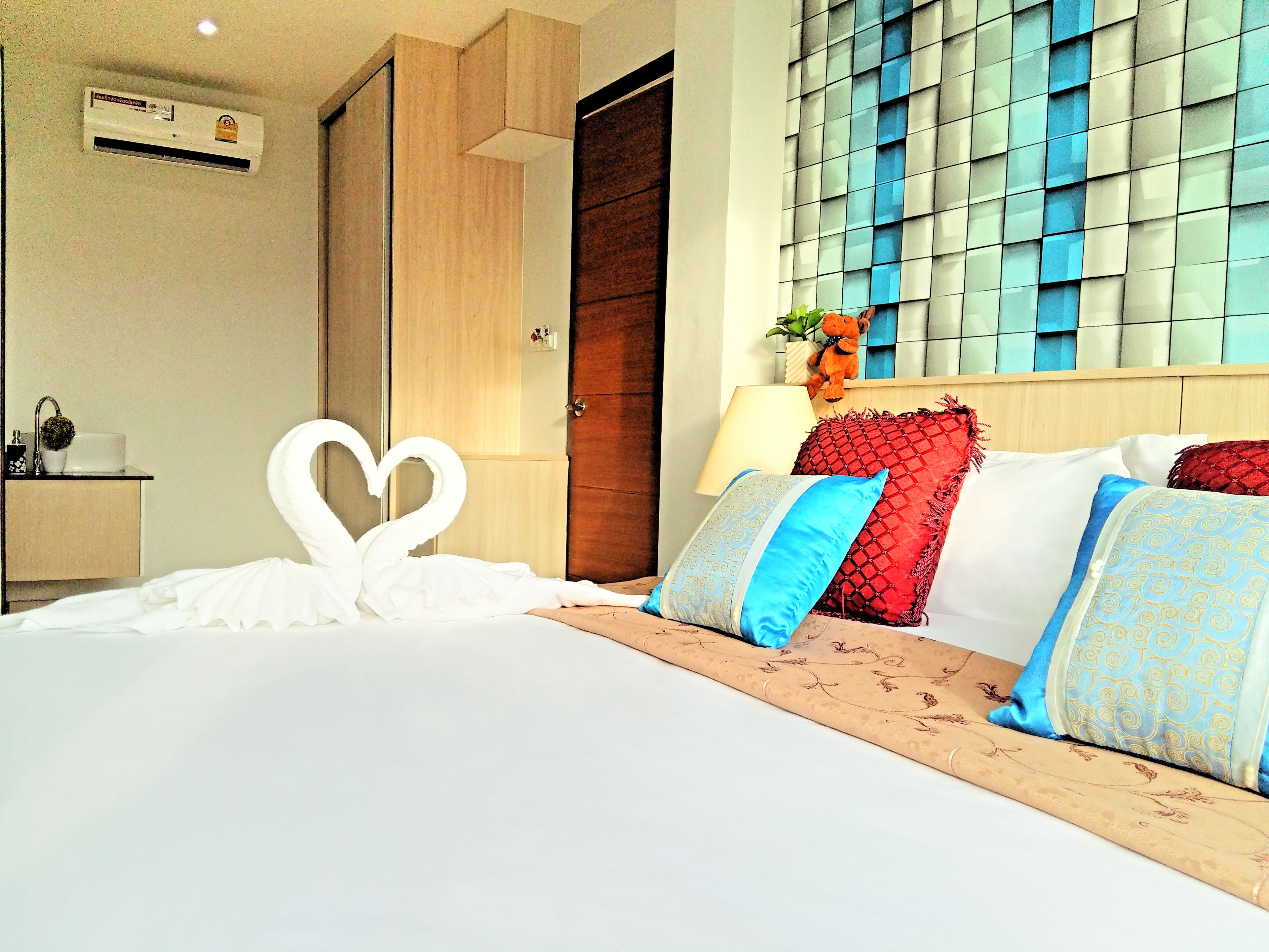 Una camera d'albergo con un letto, un comodino, un condizionatore d'aria a parete, un armadio in legno e una finestra con vista azzurra.