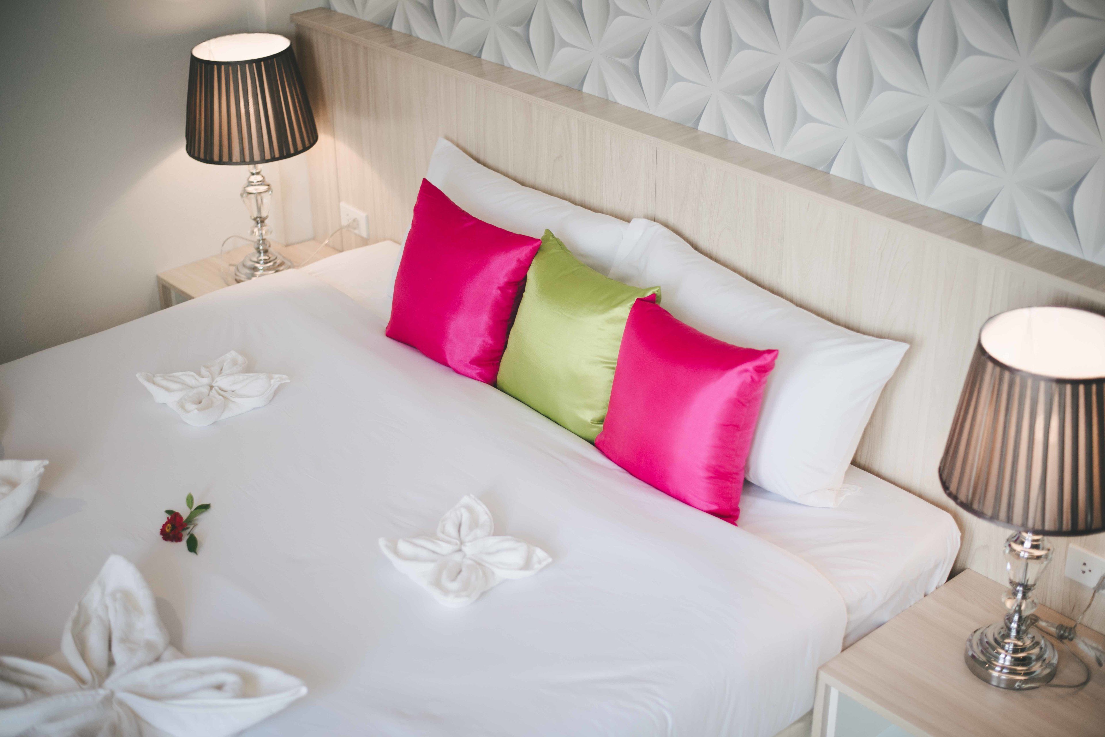 Un lit bien fait, avec du linge de lit blanc et des coussins décoratifs dans des tons de rose et de vert.