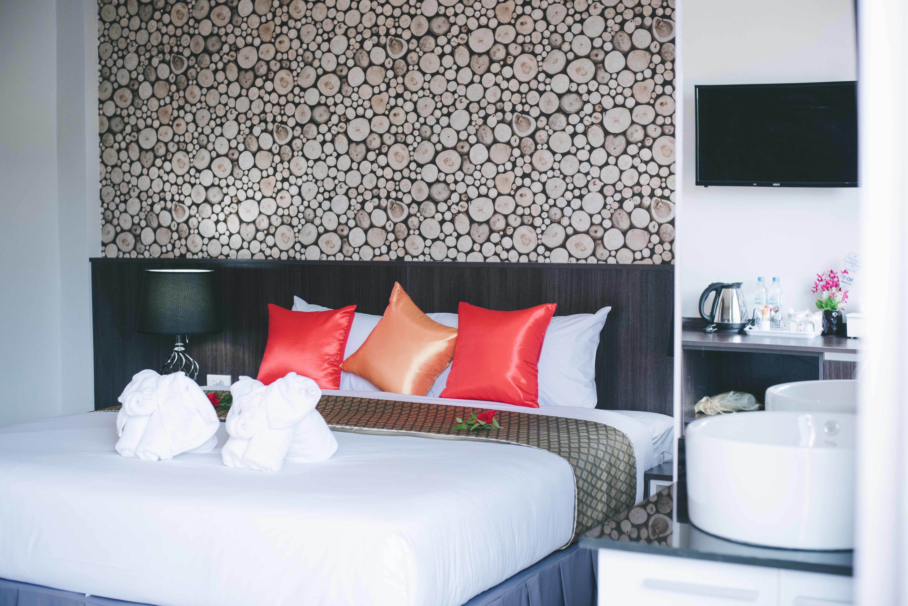 Habitación de hotel con una cama bien hecha, un televisor montado en la pared y una mesita de noche con hervidor y botellas de agua.