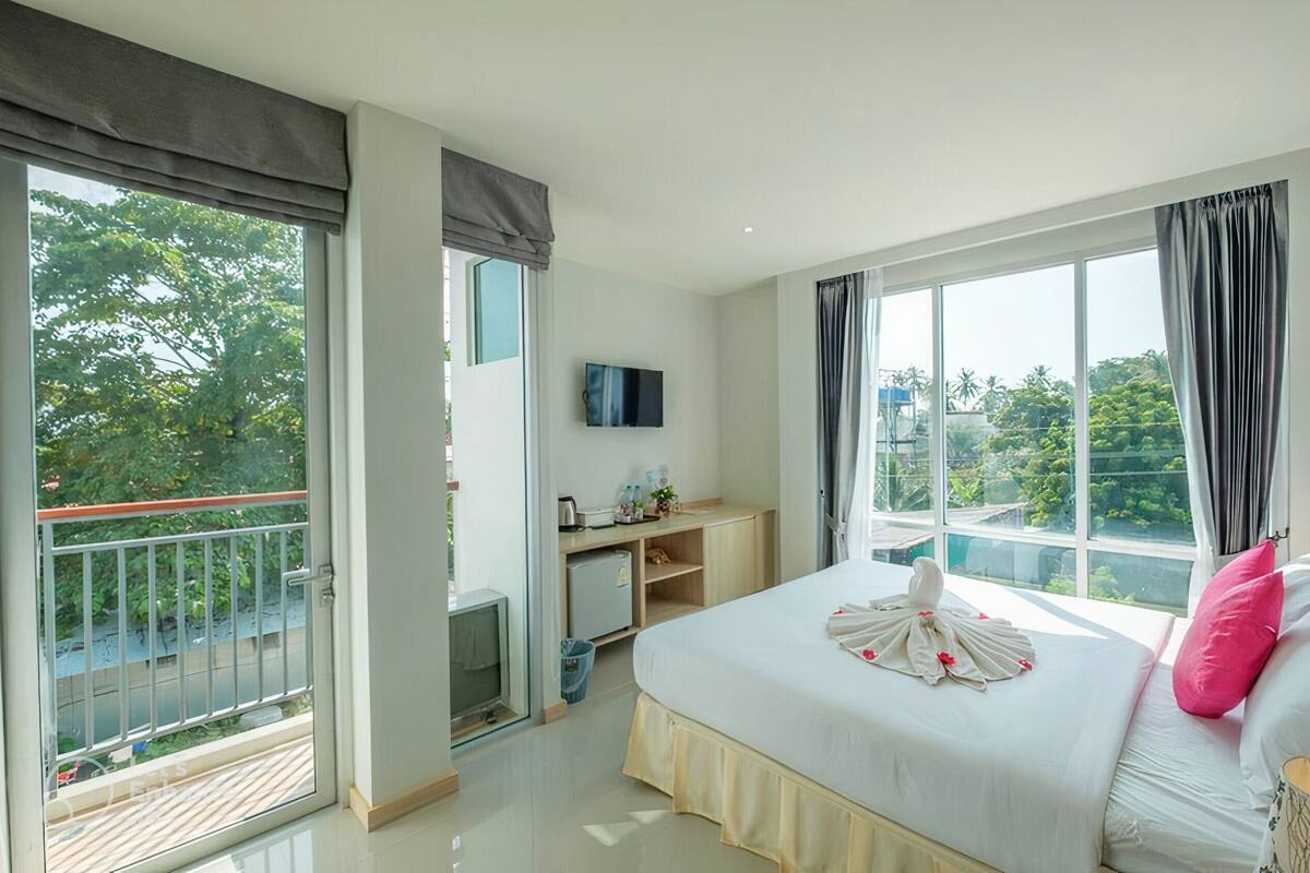 Une chambre d’hôtel avec un lit, un bureau, une télévision et un balcon donnant sur des arbres et une piscine.