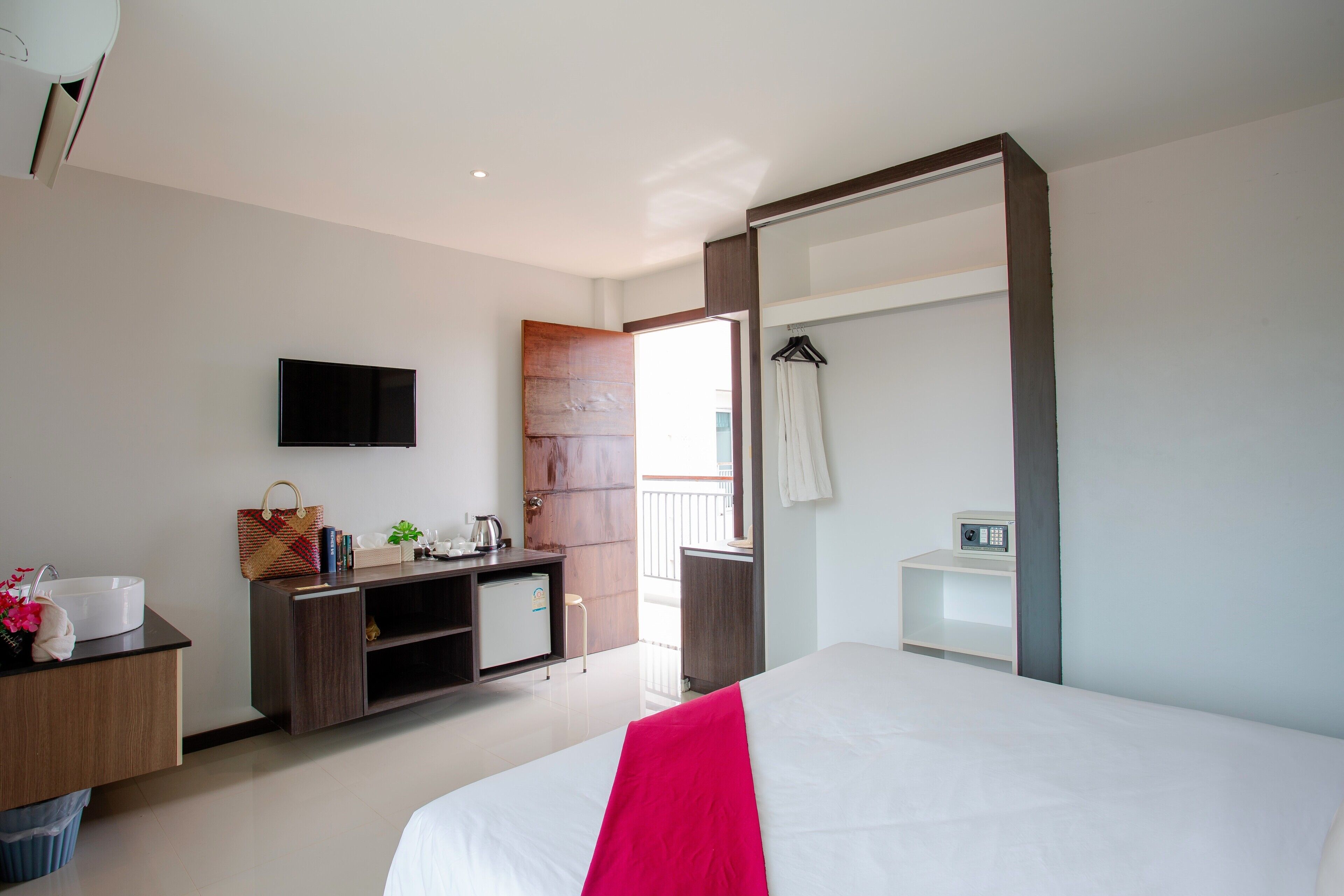 Quarto de hotel com cama, televisão, secretária com computador, pequeno espaço de cozinha e varanda.