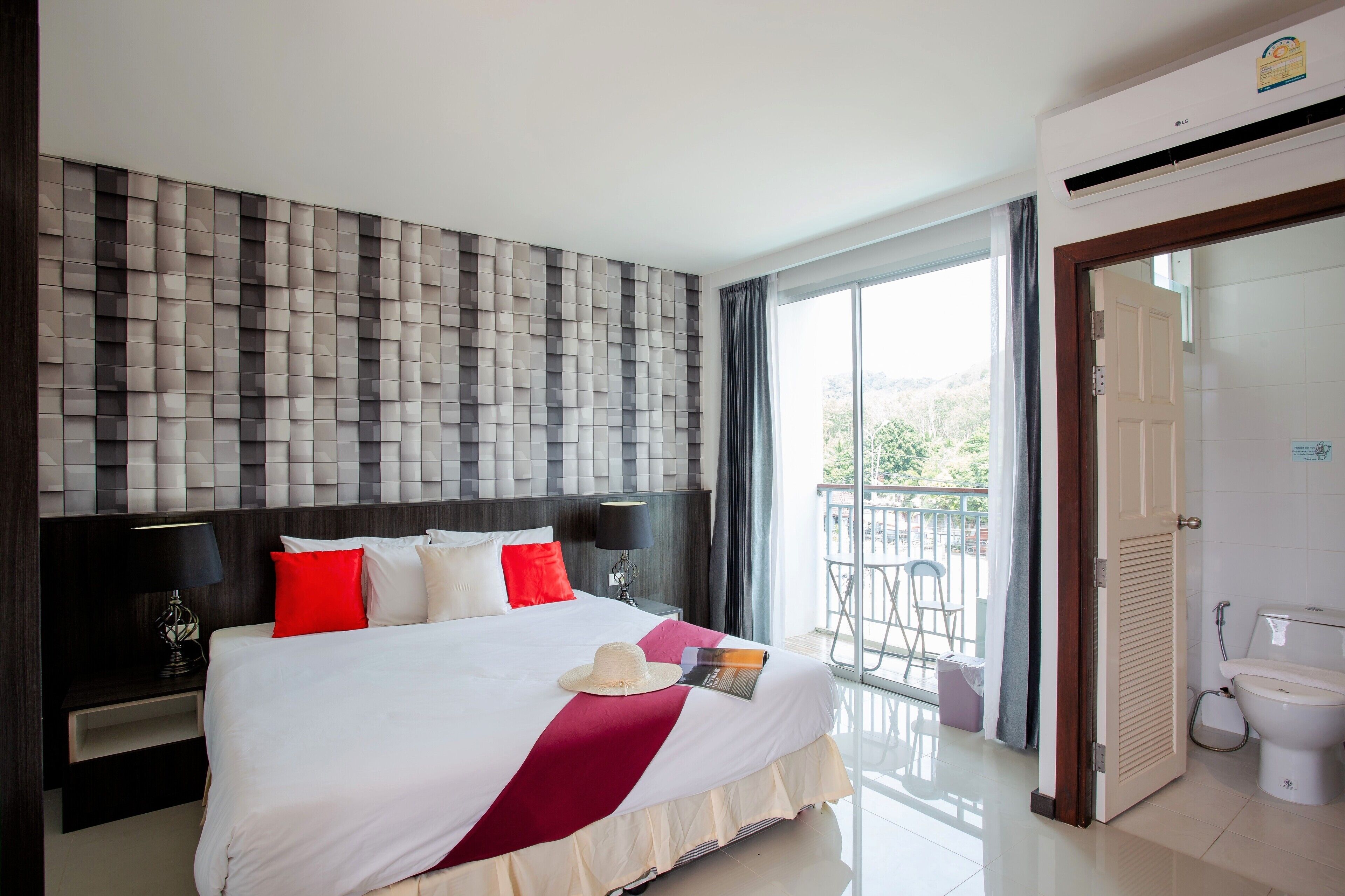Habitación de hotel con una cama grande, cabecera con diseño texturizado, mesita de noche con lámpara y vistas al exterior a través de una puerta corrediza.