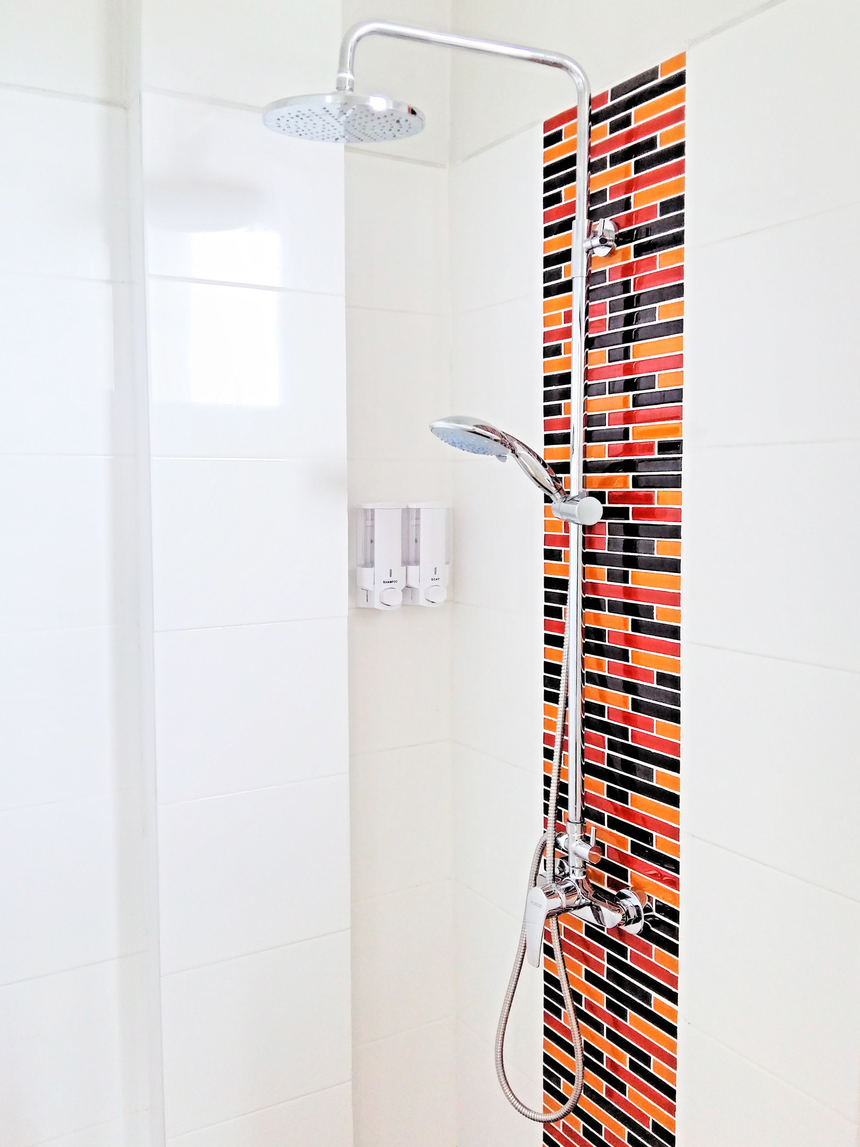 Una ducha de diseño moderno, pared con azulejos tipo ladrillo y un secamanos visible.