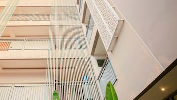 Un immeuble à plusieurs étages doté de balcons, d’un mur orné de motifs et de grandes feuilles vertes au premier plan.