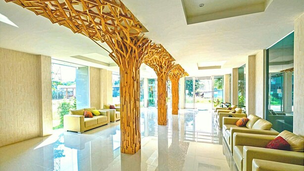 Un hall d’entrée spacieux au design moderne, avec une structure centrale en bois, des coins salon confortables et de grandes fenêtres offrant une vue sur l’extérieur.