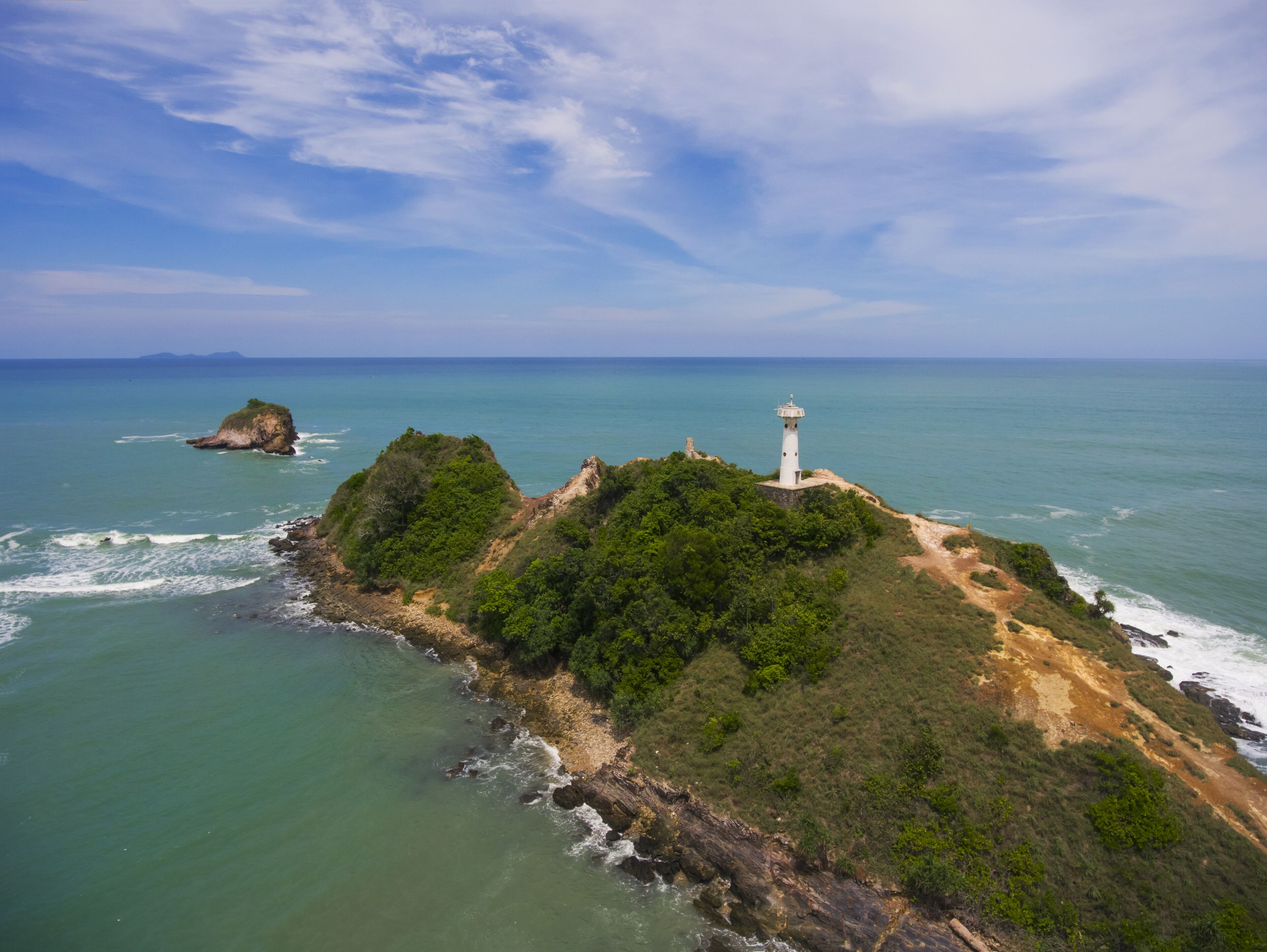 A coastal landscape with a lighthouse on a rocky outcrop, surrounded by greenery and the sea.
