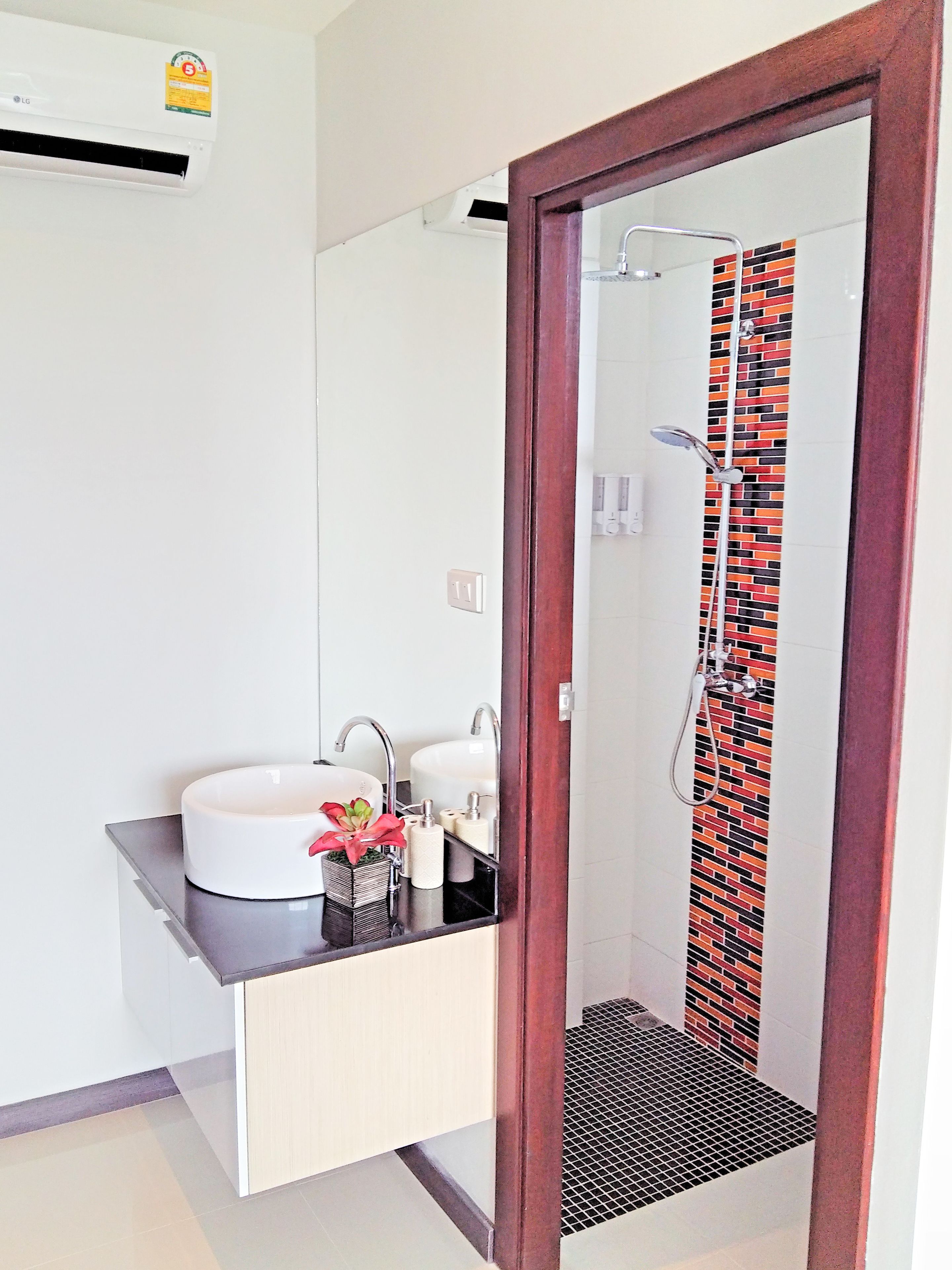 A bathroom with a white sink, two faucets, a mirror, a shower with a patterned curtain, and a small potted plant.