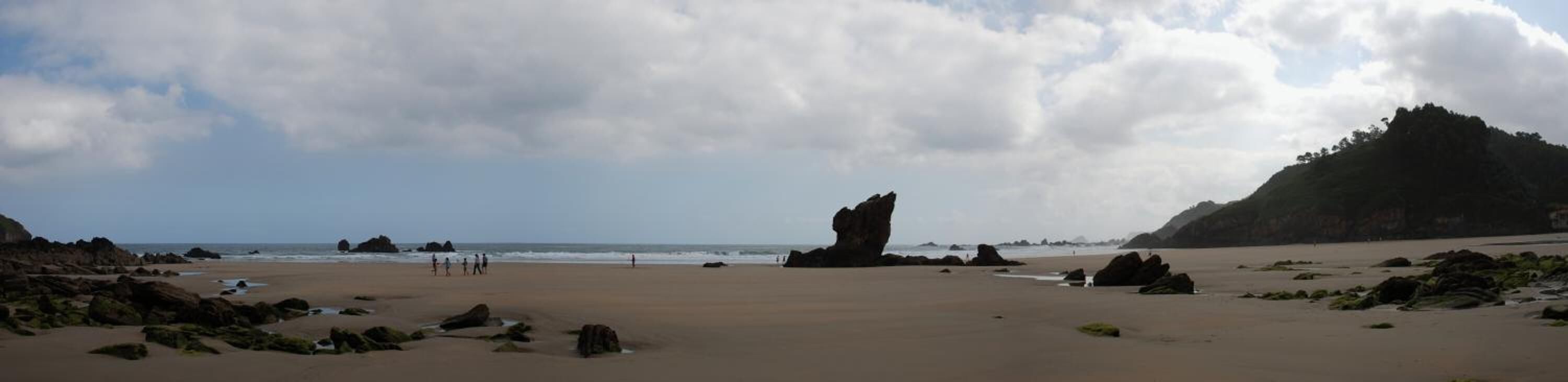 Una playa con rocas grandes, cielo despejado y una montaña a lo lejos.