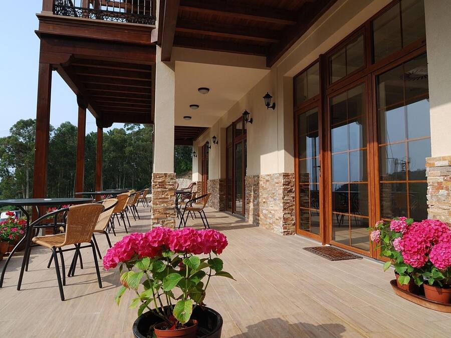 An outdoor patio with tables and chairs, potted plants, and a building with stone walls and large windows.