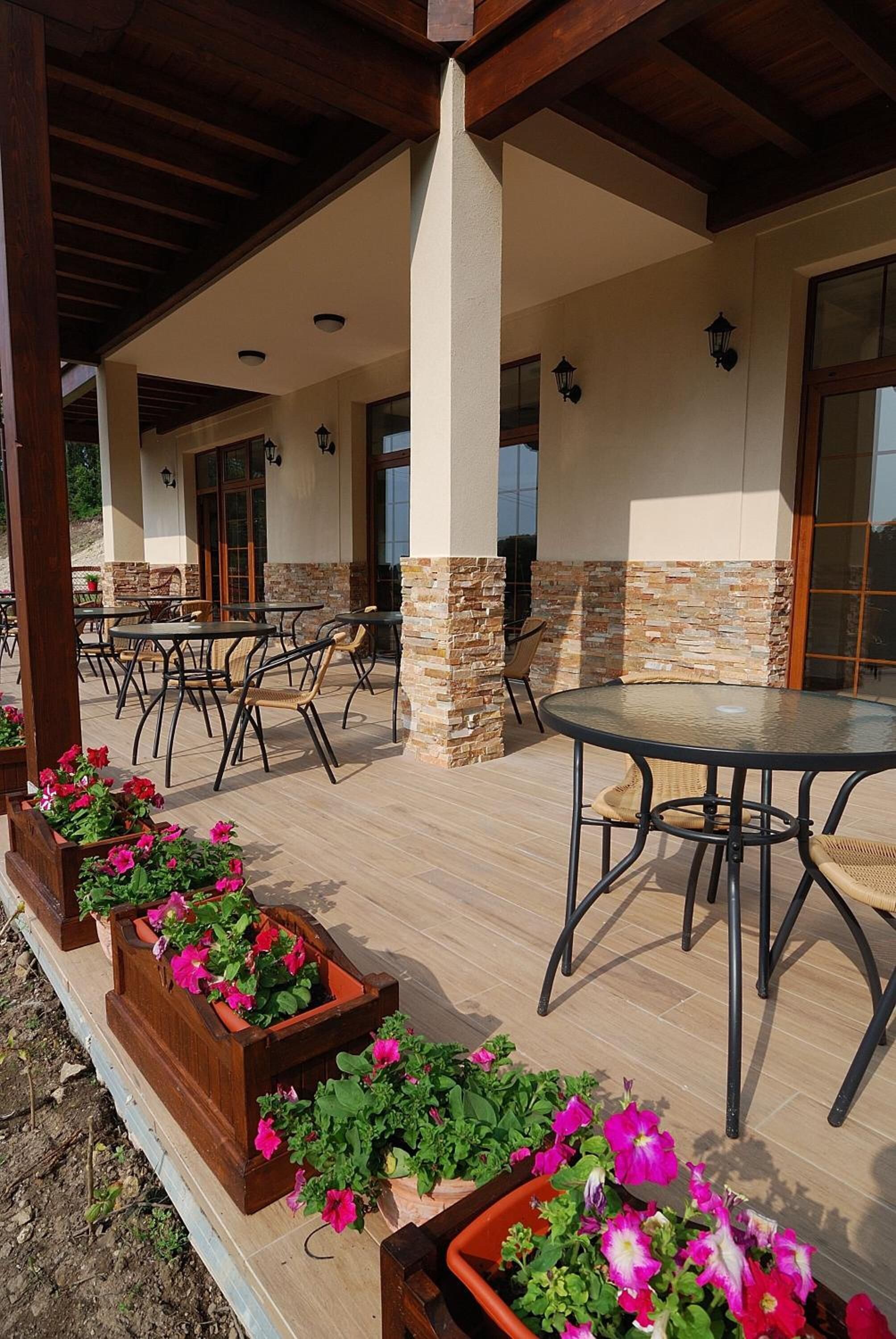 Un patio al aire libre con mesas y sillas, detalles de piedra y macetas con flores.