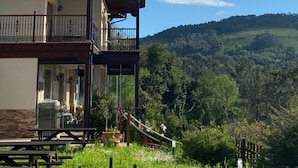 A two-story house with a balcony, a wooden deck, and a view of a forested hill.