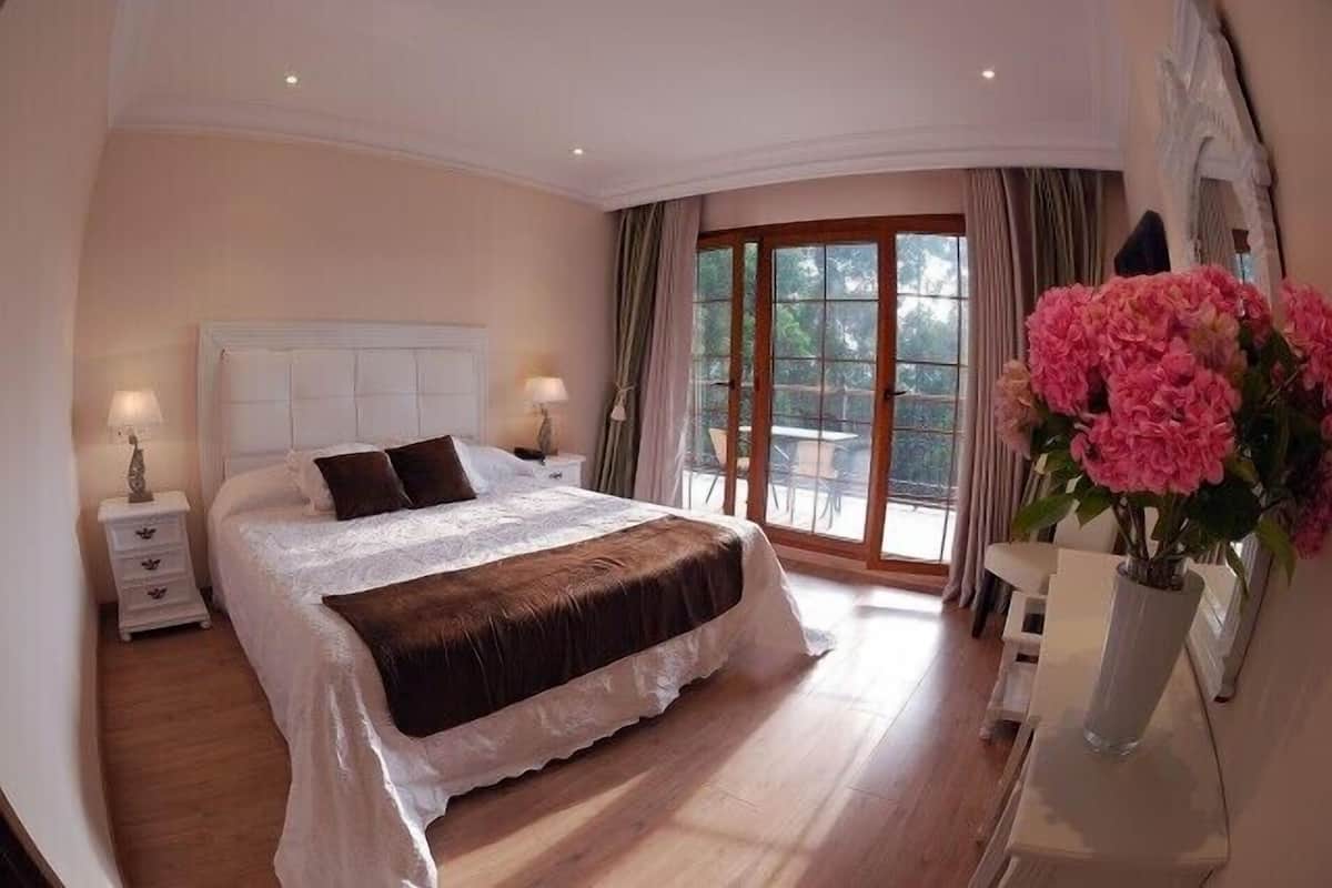 A bedroom with a large bed, a nightstand, a dresser, and a window with curtains.