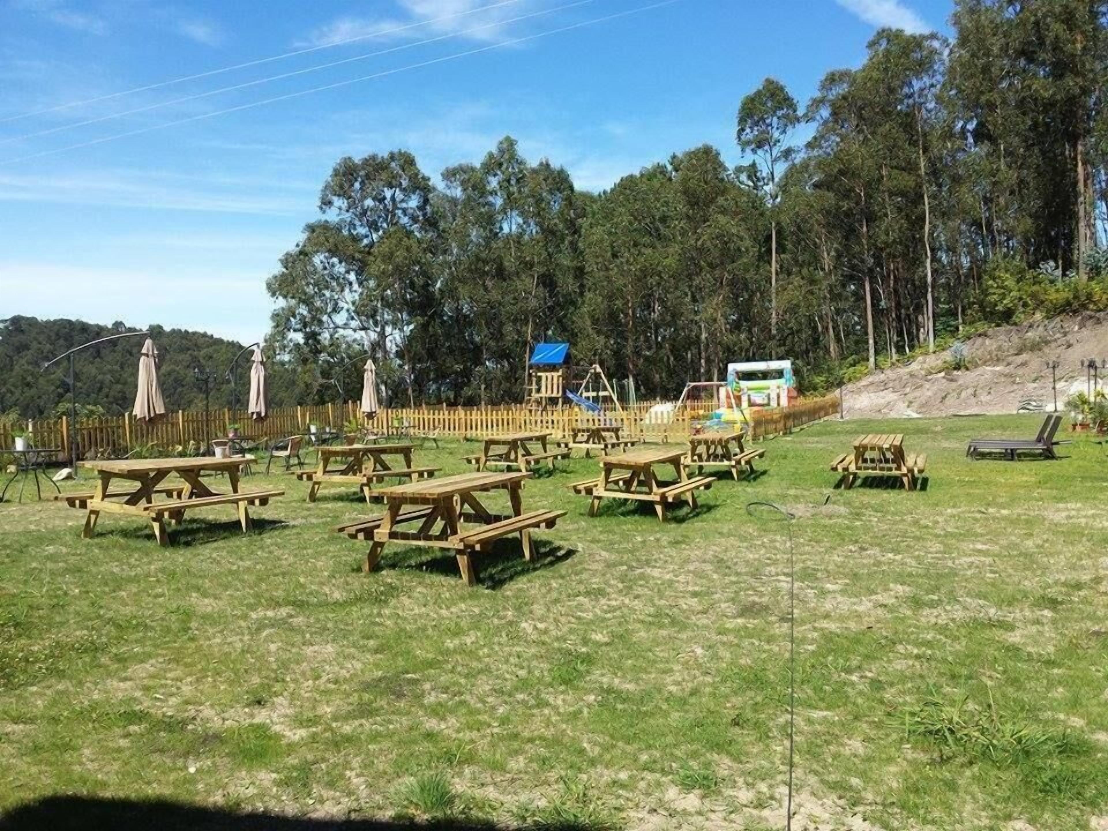 Un espacio al aire libre para picnic con varias mesas y bancos de madera, rodeado por una valla de madera y árboles.
