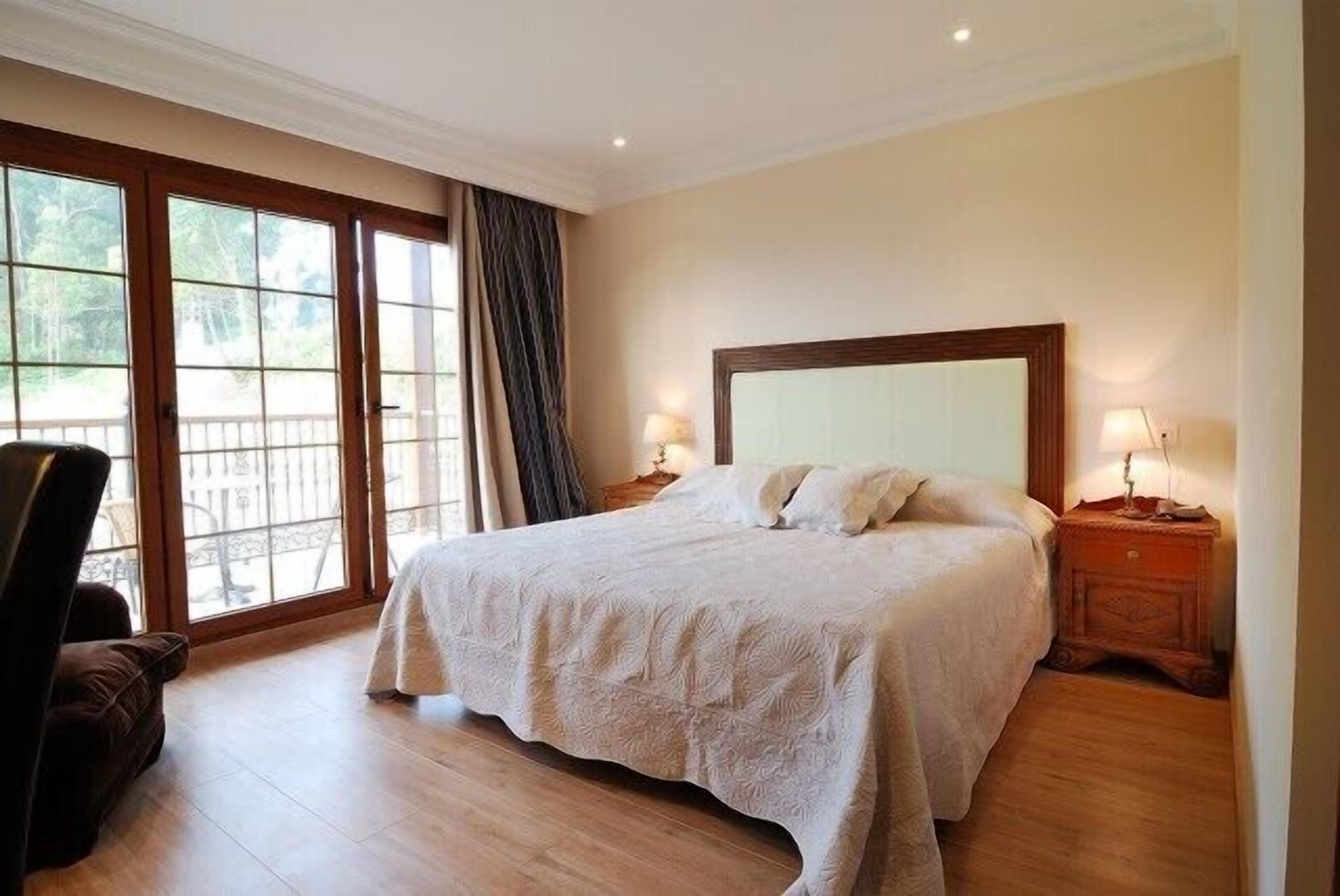 Un dormitorio espacioso con una cama grande, suelo de madera y vistas a través de un ventanal corredero.