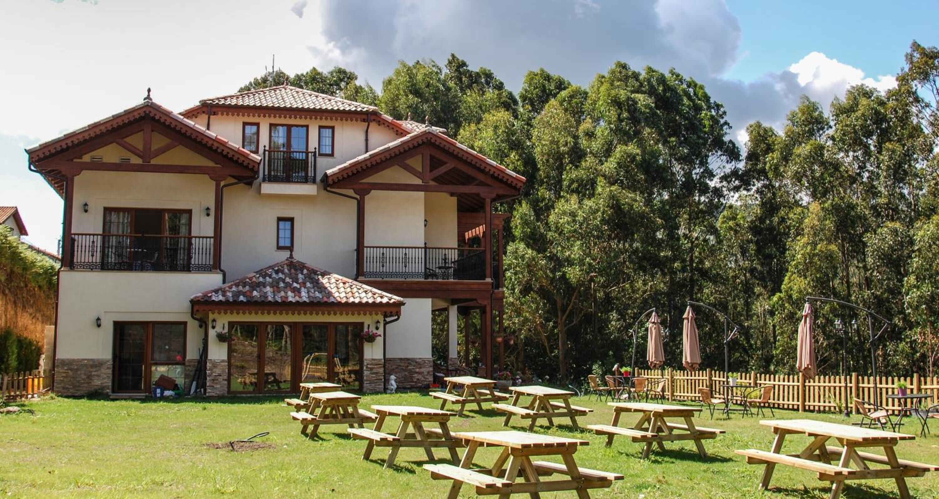 Un edificio de dos pisos con un balcón, un patio con mesas de picnic y una valla de madera.