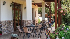 A covered patio with outdoor furniture, a wooden balcony, and a garden with various plants and flowers.