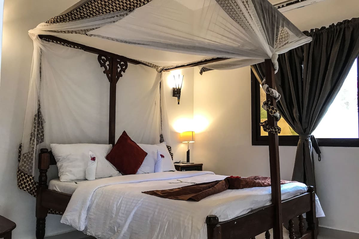Een hemelbed met witte lakens en een bruine plaid.