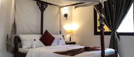 A four-poster canopy bed with white linens and a brown throw blanket.