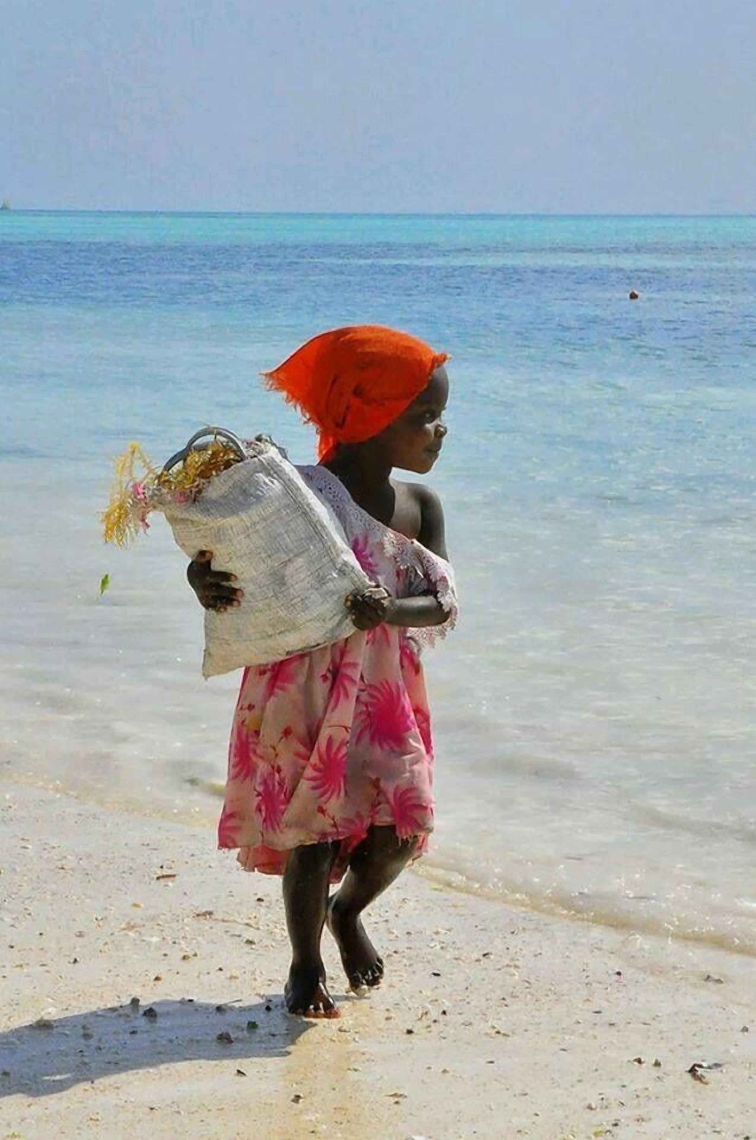 Iemand loopt over een strand met een tas vol spullen.