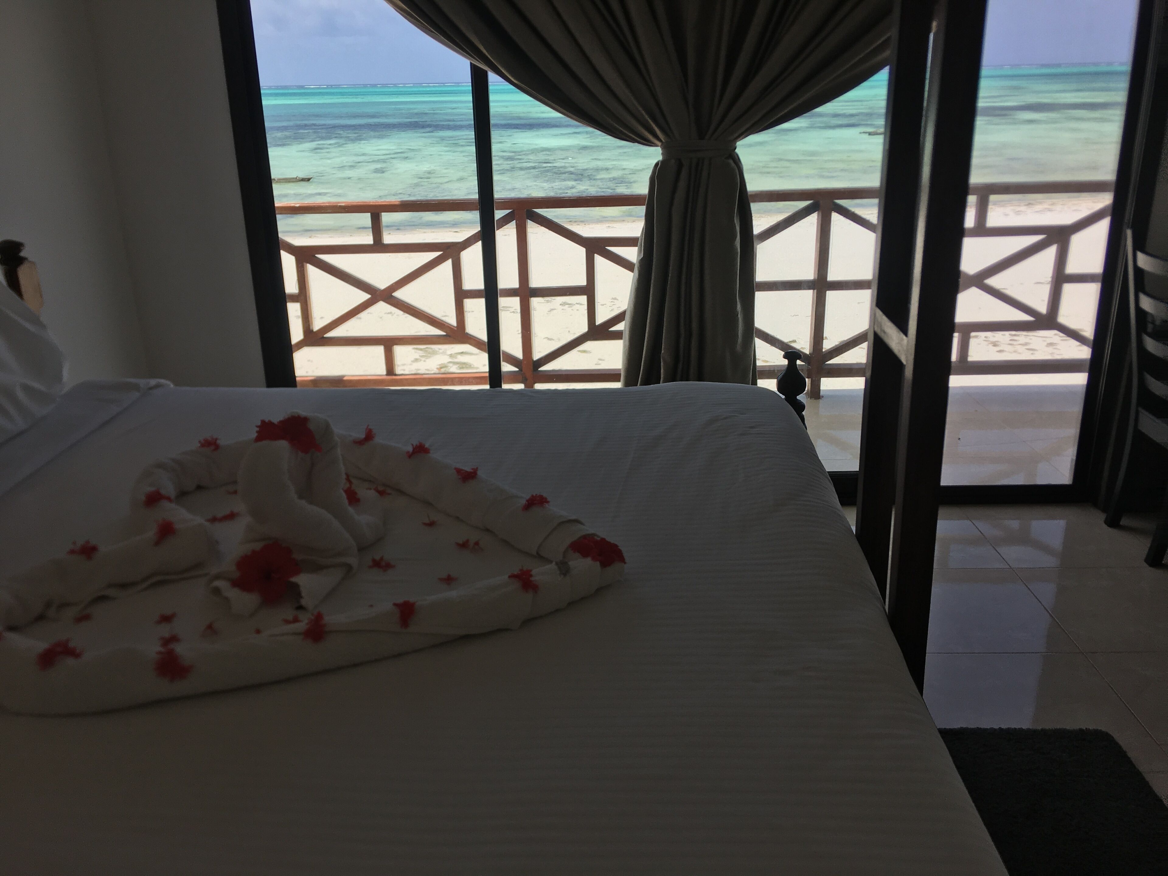A hotel room with a bed, a view of the beach, and a wooden deck.