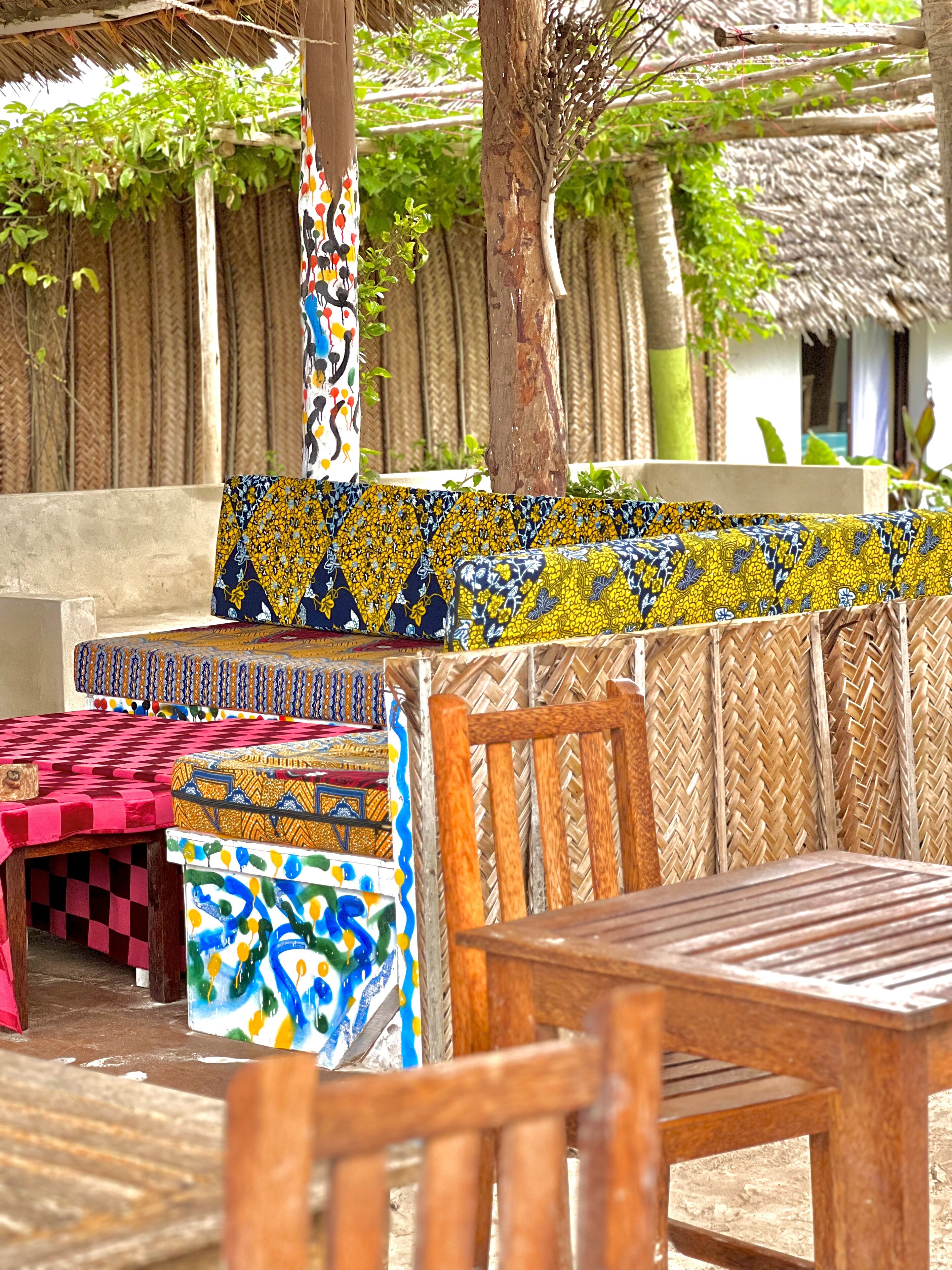 A wooden bench with a woven backrest, a table with a checkered tablecloth, and a patterned cushion.