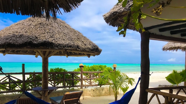 A beachside lounge with thatched umbrellas, wooden furniture, and a hammock.