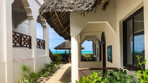 A corridor with a view of the beach, a thatched roof structure, and a wooden fence.