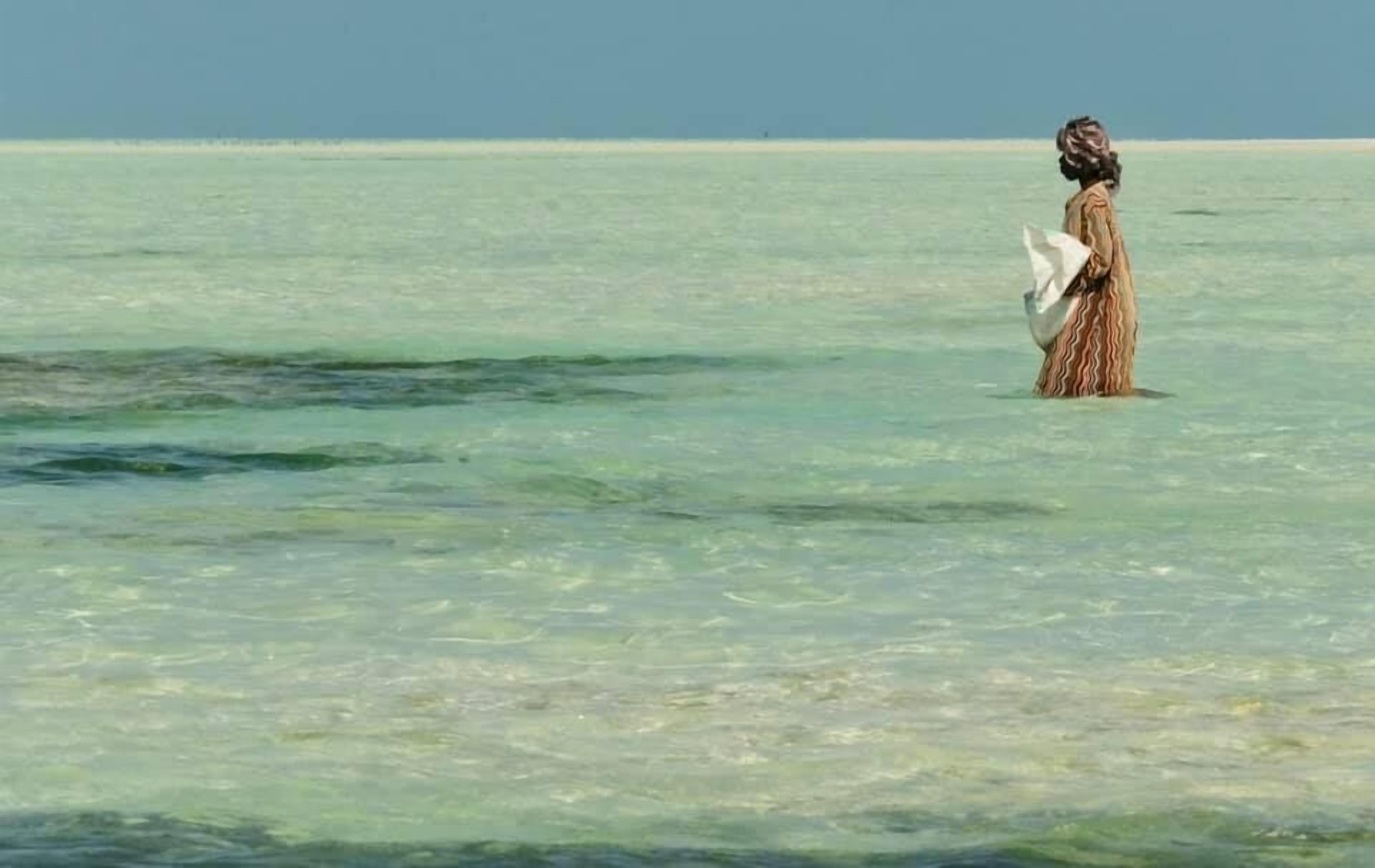A person standing in shallow water, holding a fish.