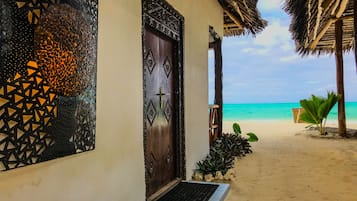 Traditional beachfront property with a thatched-roof structure and porch, surrounded by tropical plants and offering a serene beach view.