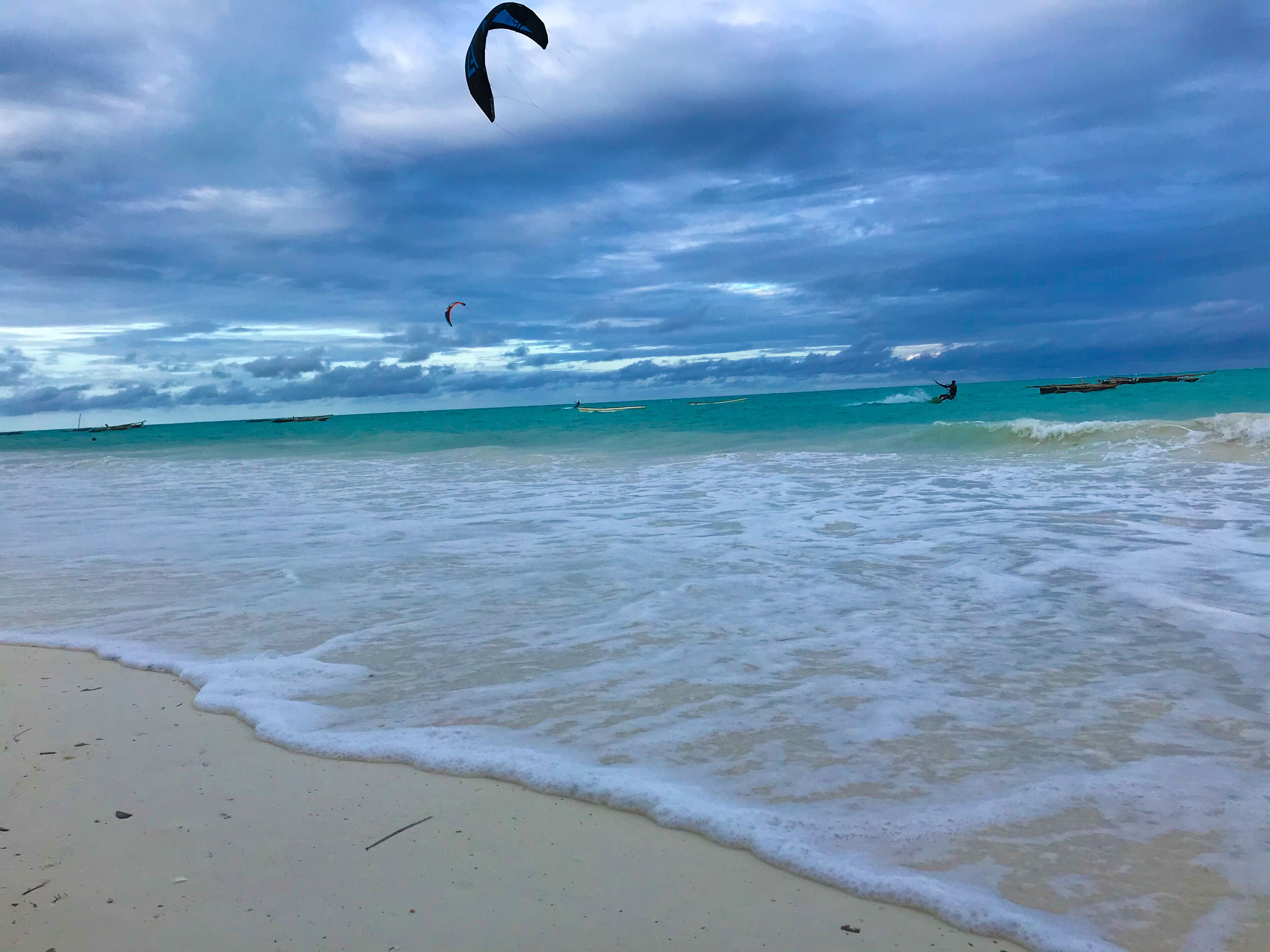 A beach with turquoise water, waves, and a kite surfer in the distance.