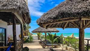A beachside resort with thatched-roof structures, lounge chairs, and a sandy pathway leading to the beach.