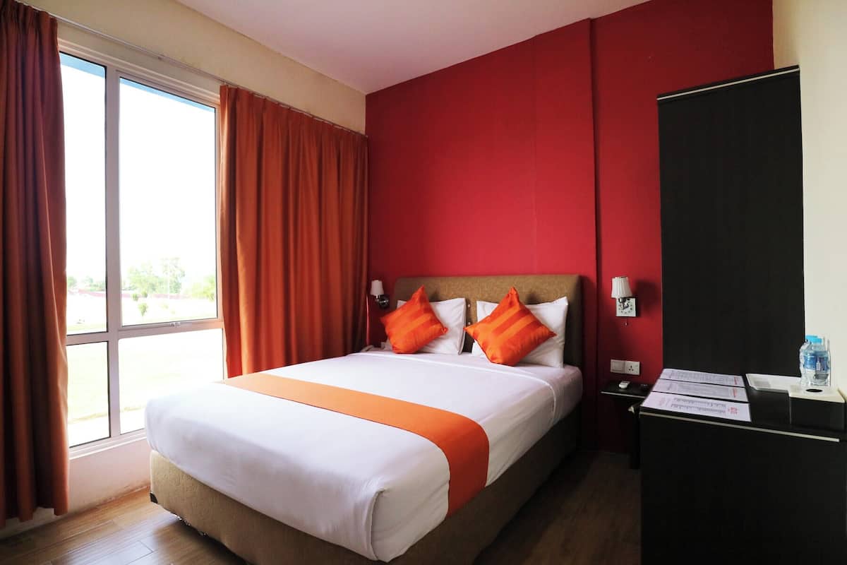 A hotel room with a bed, a desk, a chair, a window with curtains, and a red wall.