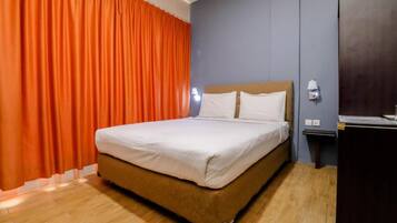 Een hotelkamer met een bed, oranje gordijnen, een nachtkastje en een aan de muur bevestigde lamp.