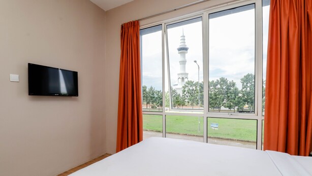 Habitación de hotel con cama, televisor de pantalla plana en la pared y un amplio ventanal con cortinas naranjas.