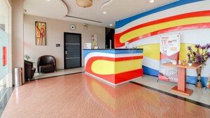 Zona de recepción de un hotel con diseño moderno, que incluye un mostrador de recepción, un reloj y una pared con un diseño abstracto y colorido.