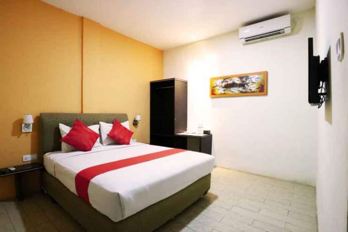 A hotel room with a bed, a nightstand, a TV, and an air conditioning unit.