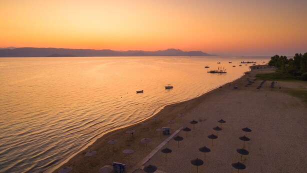 Una playa con sombrillas y un mar tranquilo al atardecer.